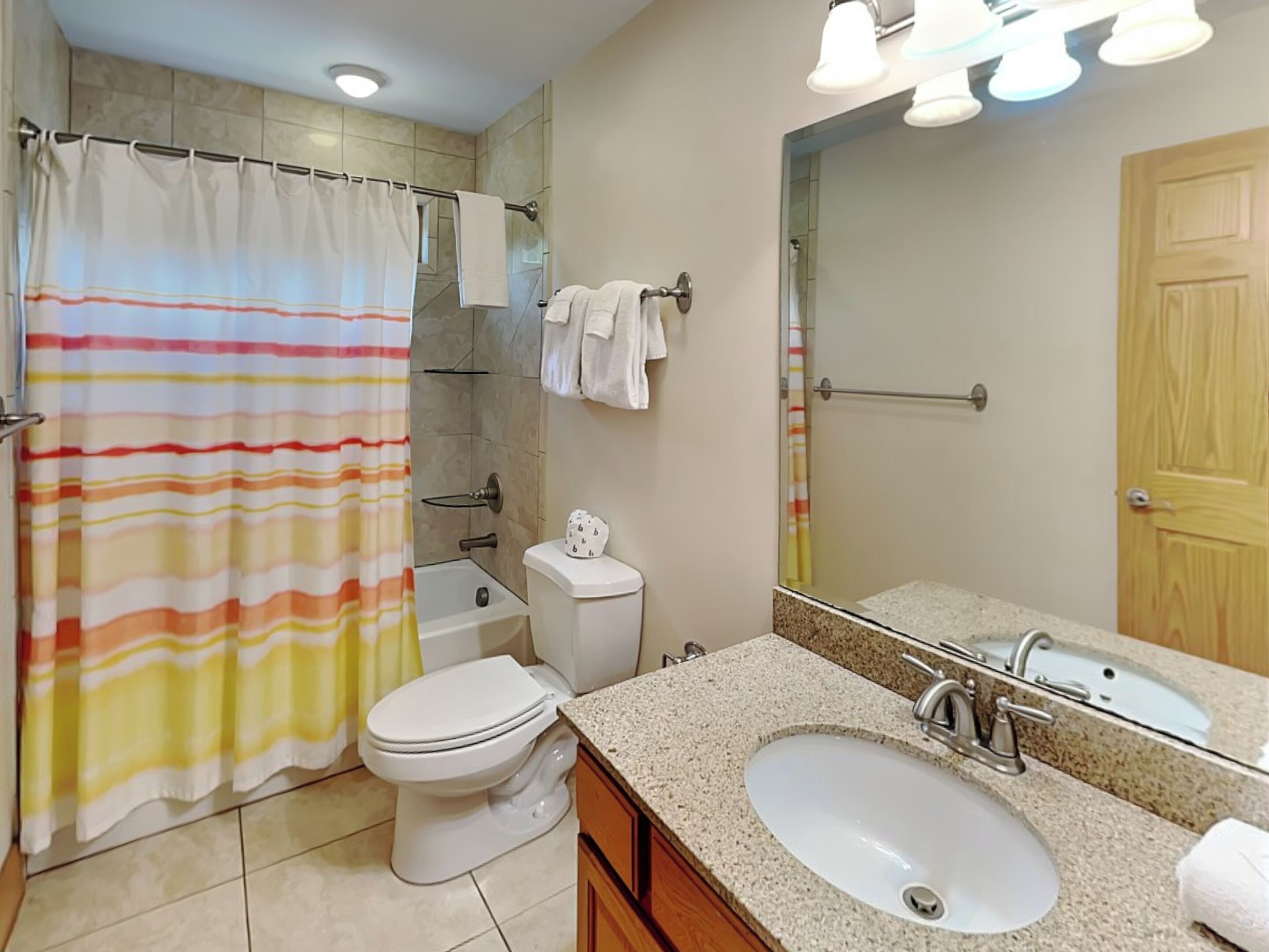 A bathroom with a shower curtain, toilet, sink, and a mirror.