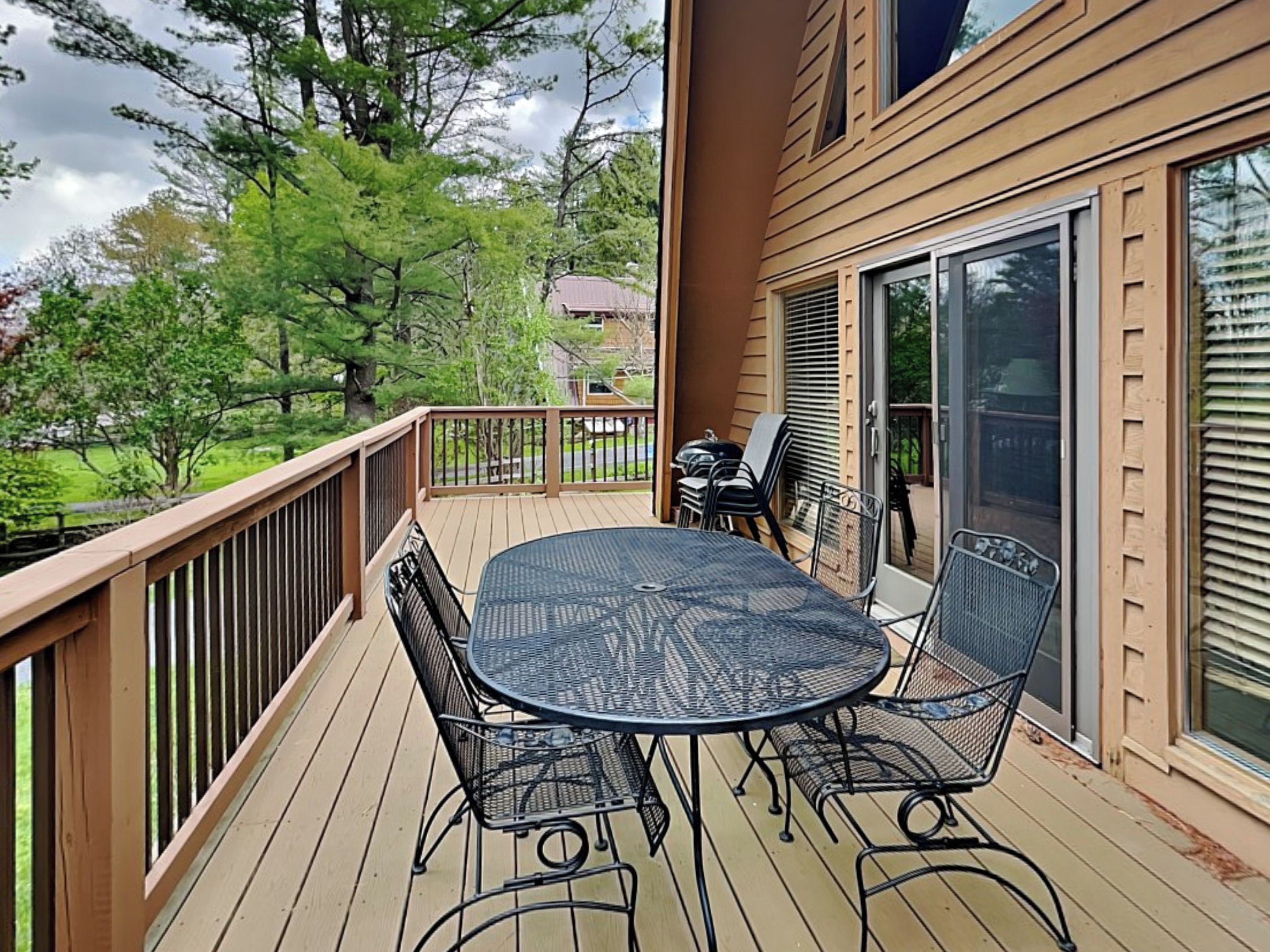 A wooden deck with a round table and chairs, a sliding glass door, and a view of a green landscape.