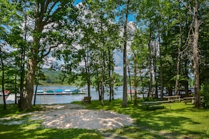 Um parque de campismo à beira do lago, com mesas de piquenique e uma área de areia.