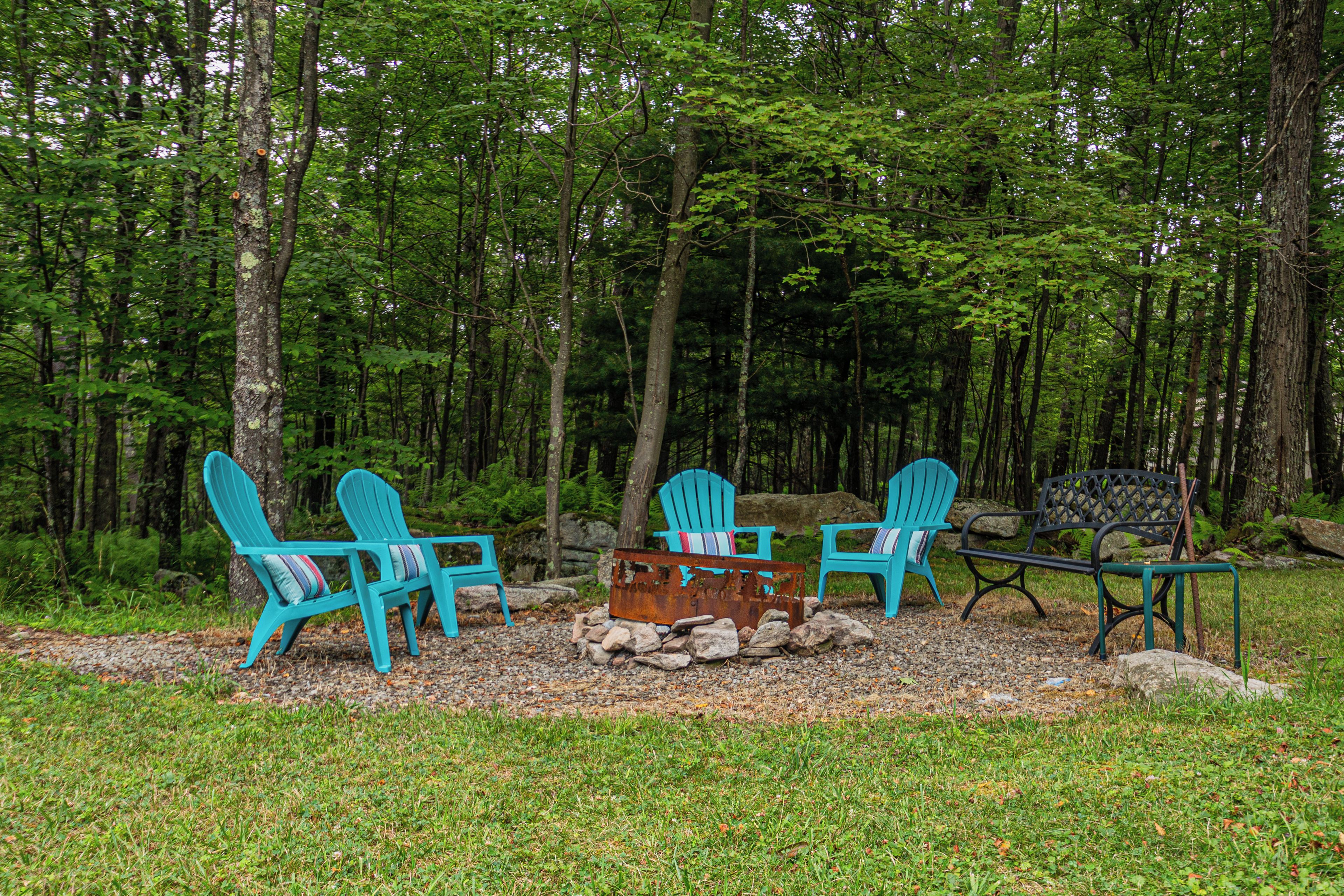 Area boscosa con un angolo relax con due poltrone Adirondack e una panchina, circondato da rocce e vegetazione.