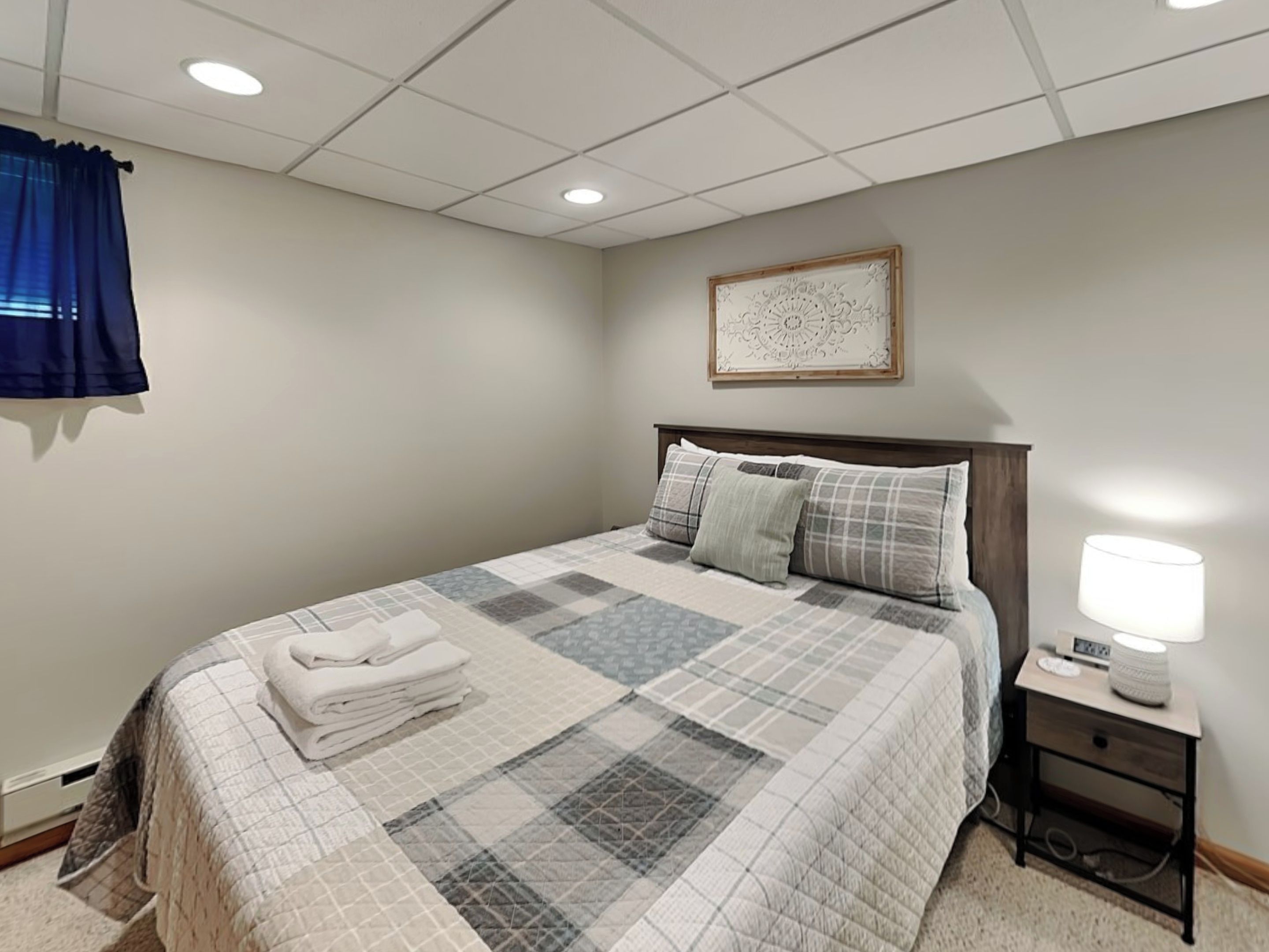 A neatly made bed with a quilt, a bedside lamp, and a small bedside table with a lamp.