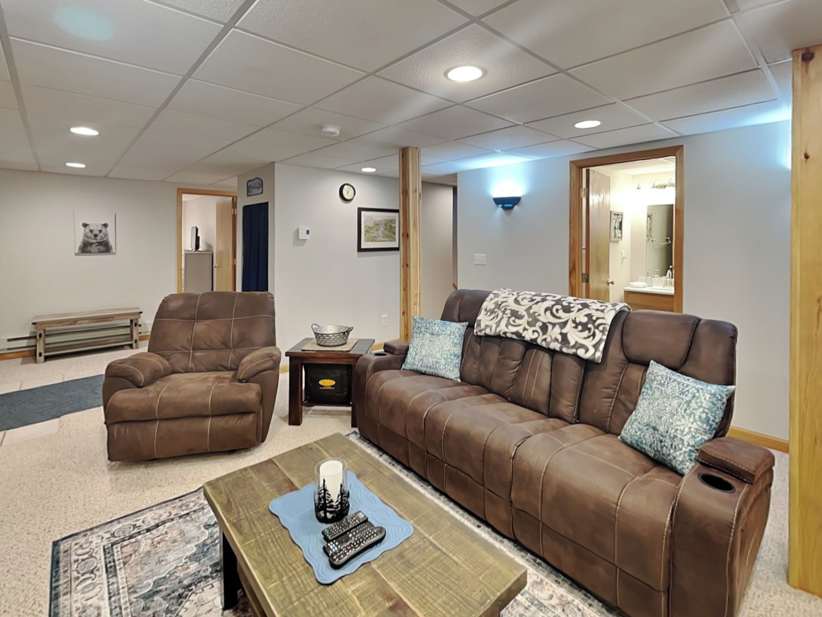 A living room with a brown leather sofa, a brown leather armchair, a wooden coffee table, and a small side table with a lamp.