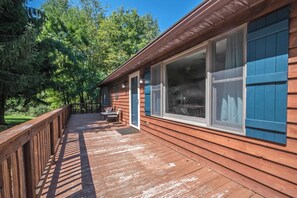 A wooden deck with a railing, a table, and chairs, leading to a building with large windows and blue shutters. - Laurel Ridge by Taylor Made Deep Creek (McHenry)