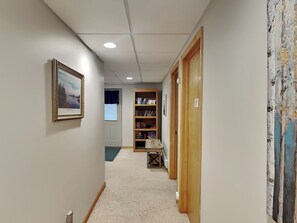 A hallway with a carpeted floor, a wooden bookshelf, and a door with a curtain. - Laurel Ridge by Taylor Made Deep Creek (McHenry)
