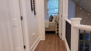 A hallway with wooden flooring, white walls, and a loft bedroom with a window. - Lazy Days by Taylor Made Deep Creek (McHenry)