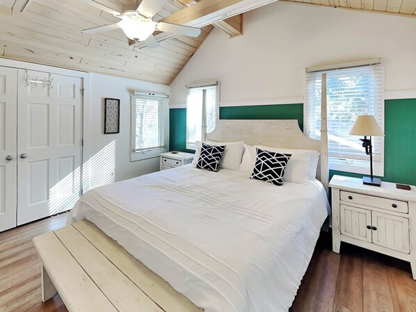 Ein Schlafzimmer mit einem großen Bett, einer Bank, einem Deckenventilator und einem Fenster mit Jalousien.