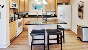 A modern kitchen with wooden cabinets, a central island with bar stools, a refrigerator, and a microwave. - Lazy Days by Taylor Made Deep Creek (McHenry)