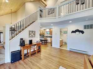 A spacious living area with a wooden floor, a staircase with a railing, a kitchen with wooden cabinets, and a dining area with a table and chairs. - Lazy Days by Taylor Made Deep Creek (McHenry)