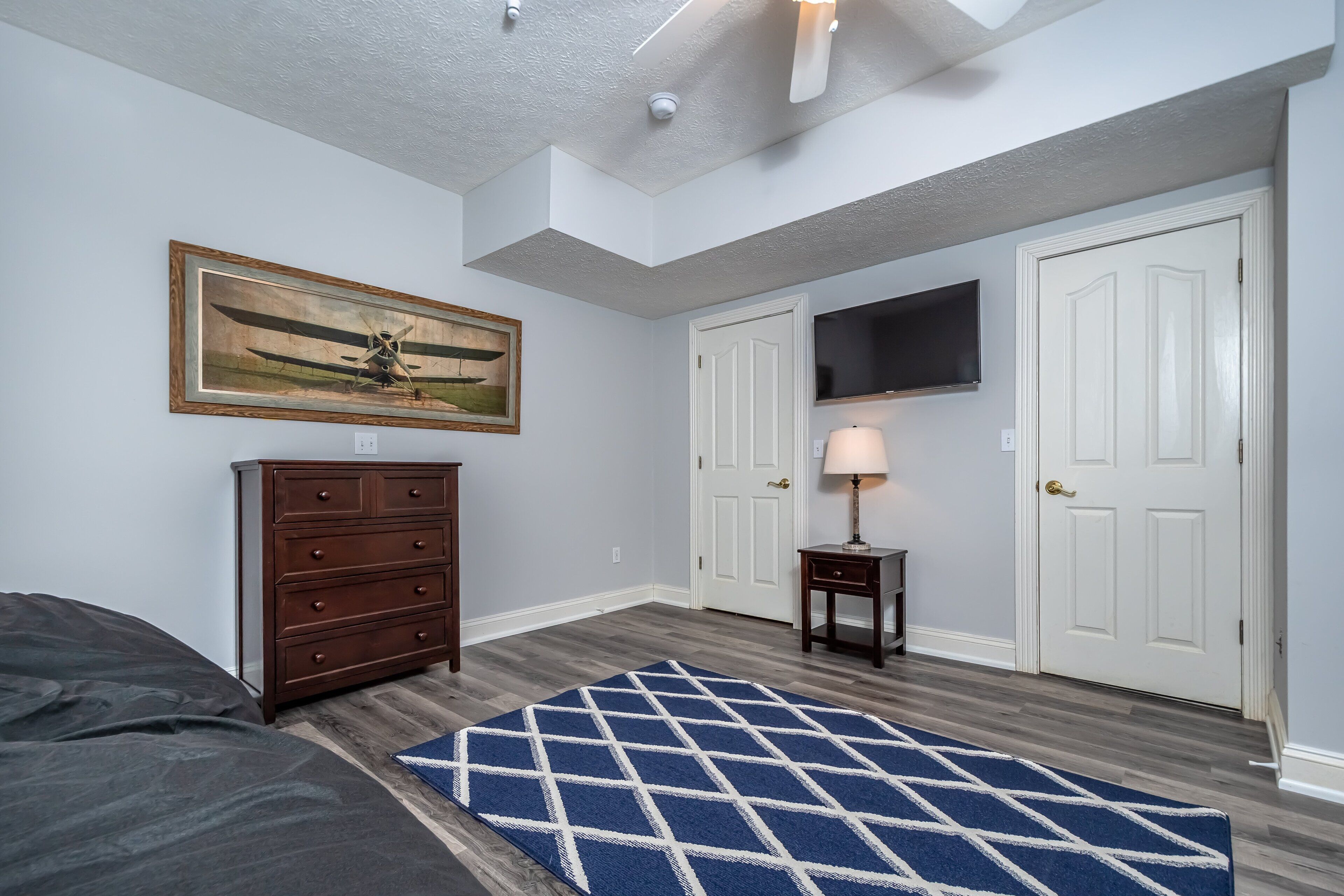 A bedroom with a bed, dresser, TV, and two doors.