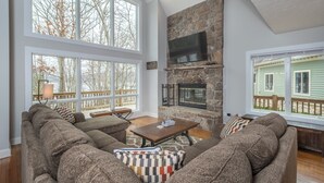 A spacious living room with a stone fireplace, large windows, and a cozy seating area. - Leap Away by Taylor Made Deep Creek (Oakland)