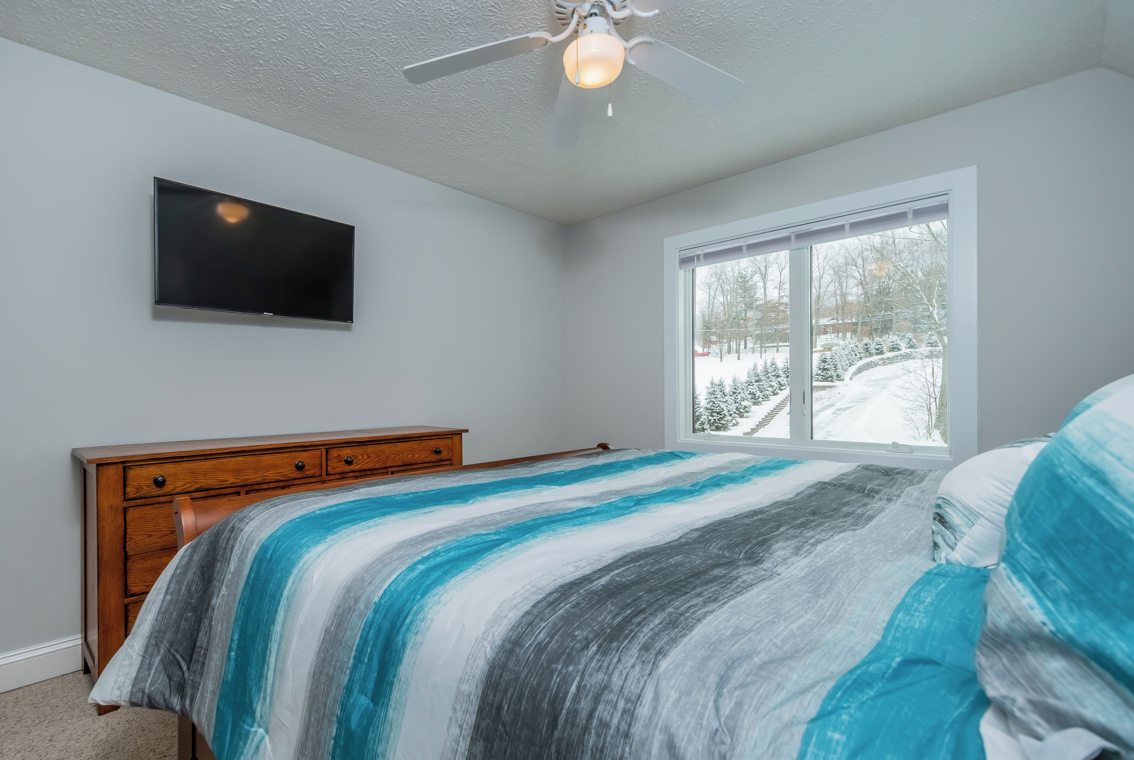 Een slaapkamer met een bed, een houten dressoir, een plafondventilator, een televisie en een raam met uitzicht op sneeuw.