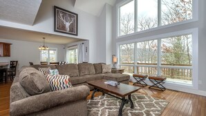 A spacious living room with a sectional sofa, a wooden coffee table, and large windows offering a view of the outdoors. - Leap Away by Taylor Made Deep Creek (Oakland)