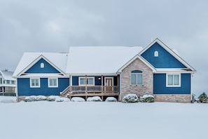 A two-story house with a stone foundation and blue siding, featuring a front porch and a covered deck.