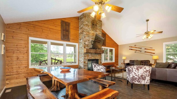 A rustic interior with a wooden dining table, benches, a stone fireplace, and a ceiling fan.