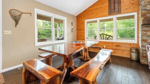 A dining area with wooden tables and benches, large windows with a view of greenery, and a rustic wooden wall.