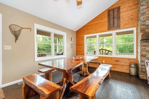A dining area with wooden tables and benches, large windows with a view of greenery, and a rustic wooden wall. - Light My Fire by Taylor Made Deep Creek (McHenry)