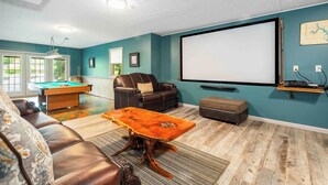 A living room with a pool table, leather sofa, and a projector screen.