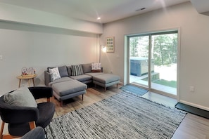 A modern living room with a sectional sofa, a small side table, and a large sliding glass door leading to a balcony. - Limestone Chalet by Taylor Made Deep Creek (McHenry)