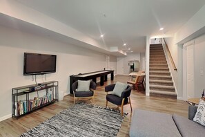 A modern living room with a flat-screen TV, a pool table, and a staircase leading to another level. - Limestone Chalet by Taylor Made Deep Creek (McHenry)
