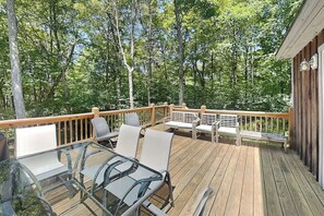 Une terrasse en bois, dotée de tables et de chaises à plateaux en verre, entourée d’une forêt.
