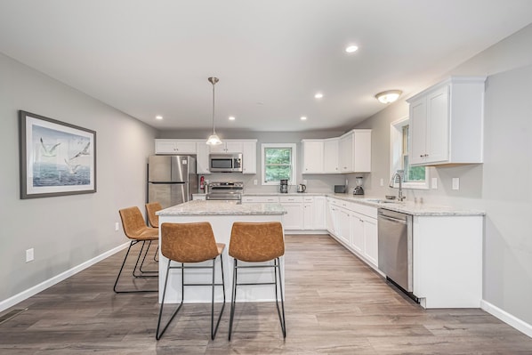 A modern kitchen with white cabinets, a central island, and a dining area with three chairs.