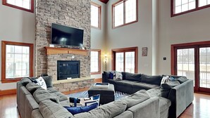 Una amplia sala de estar con chimenea de piedra, un televisor de pantalla plana grande y un sofá modular.
