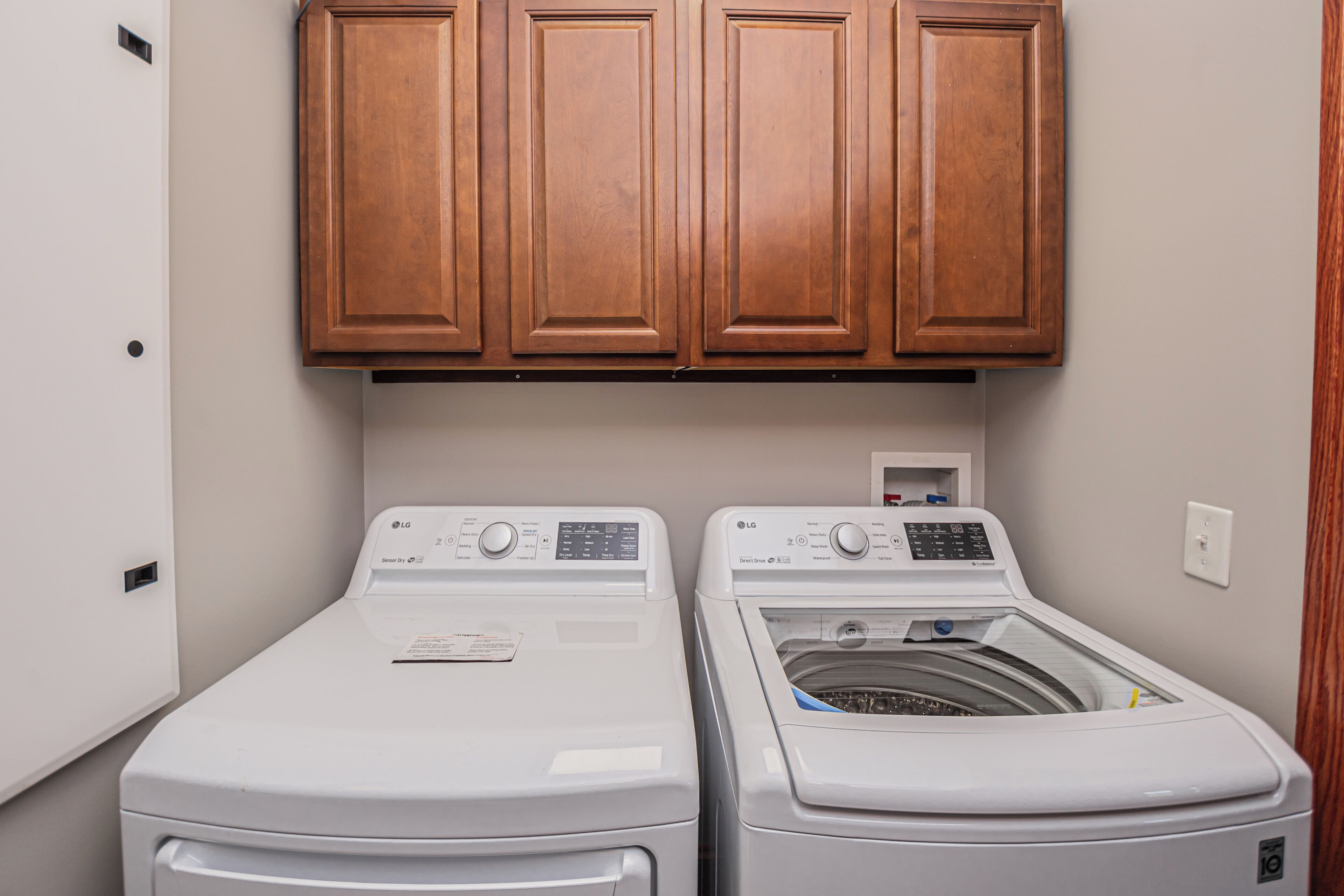 A laundry area with two white front-loading washing machines and a dryer, above which are wooden cabinets.