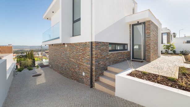 Una casa moderna con fachada de piedra, un balcón de cristal y vistas despejadas del paisaje circundante.