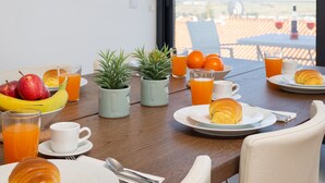 Una mesa de desayuno con cruasanes, fruta y jugo, una planta en maceta y vistas al exterior.