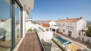 Un balcón con vistas a una piscina, edificios cercanos y cielo despejado.