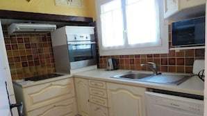 Een kleine keuken met witte keukenkastjes, een ingebouwde oven, een magnetron en een spoelbak.