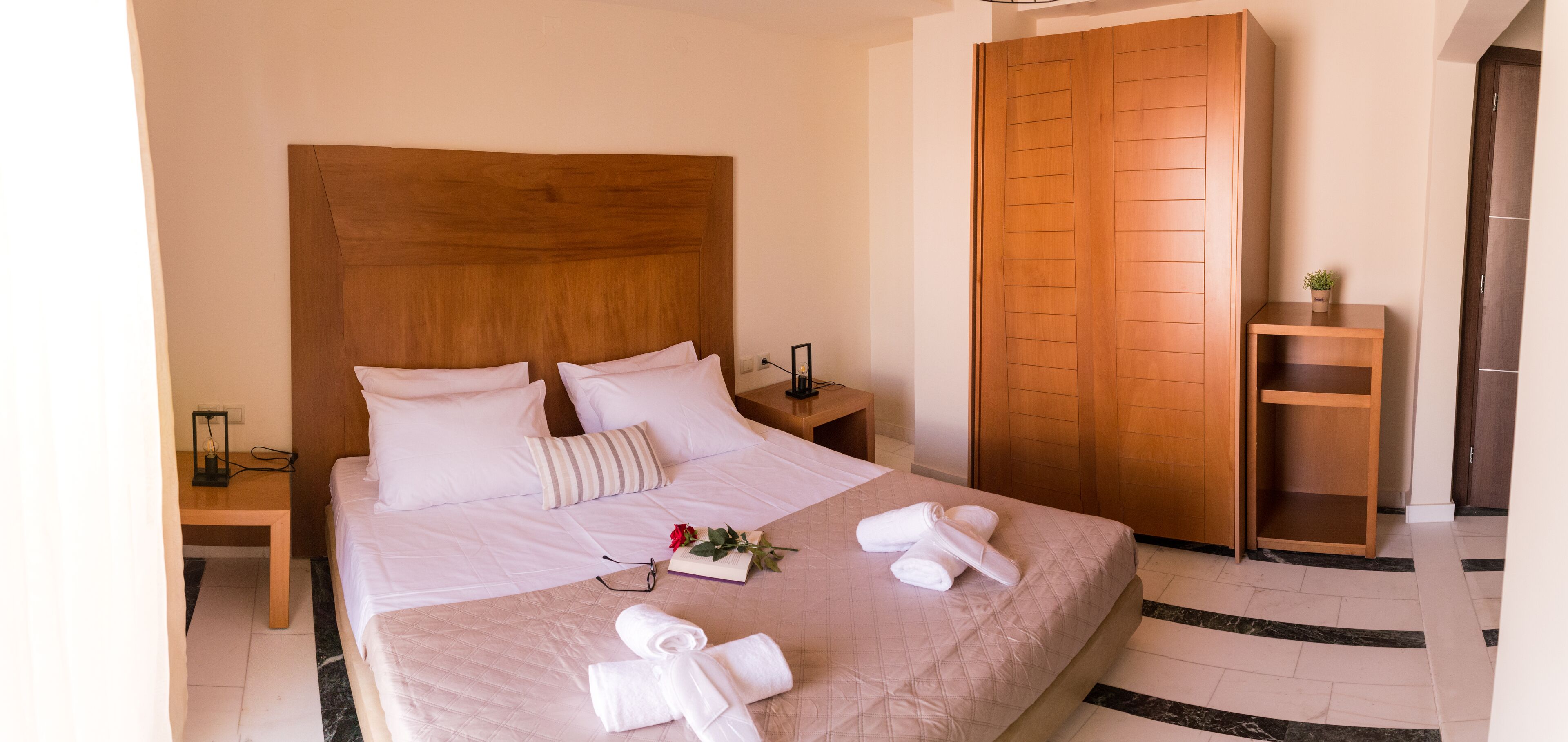 A neatly made bed with white linens, a wooden headboard, and a bedside table with a lamp and a small plant.