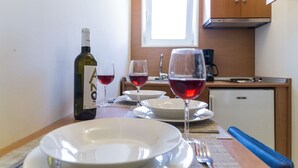 A small kitchenette with a window, a refrigerator, and a dining table set with wine glasses and plates.