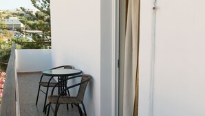 A balcony with a table and chairs, a view of buildings and greenery, and a sliding glass door.