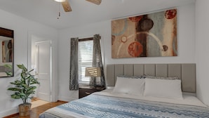 Een slaapkamer met een groot bed, een plafondventilator, een schilderij en een potplant.