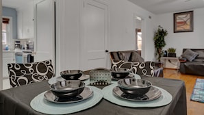 Een eetruimte met een tafel gedekt voor vier personen, stoelen met gestreepte kussens, en een keuken in de achtergrond.