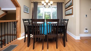 A dining area with a wooden table and chairs, a chandelier, and two framed pictures on the wall. - Live a Little by Taylor Made Deep Creek (McHenry)