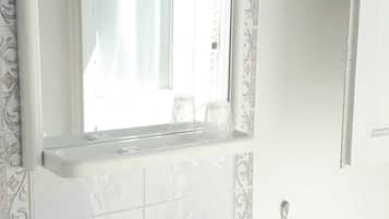 A bathroom with a white sink, two faucets, a mirror with a decorative frame, and a towel ring.