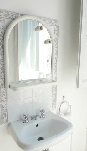 Un baño con un lavamanos blanco, dos grifos, un espejo con marco decorativo y un tozaleta.
