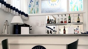Zona de bar con dos taburetes metálicos, una barra que exhibe varias botellas y un ventanal con el logotipo 'Hotel Rex'.
