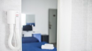 Habitación de hotel con un secador blanco de pared, una cama con cubrecama azul, un televisor y una puerta.