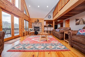 A spacious living room with a fireplace, wooden furniture, and a large rug. - Duck Pond Lodge by Taylor Made Deep Creek (McHenry)