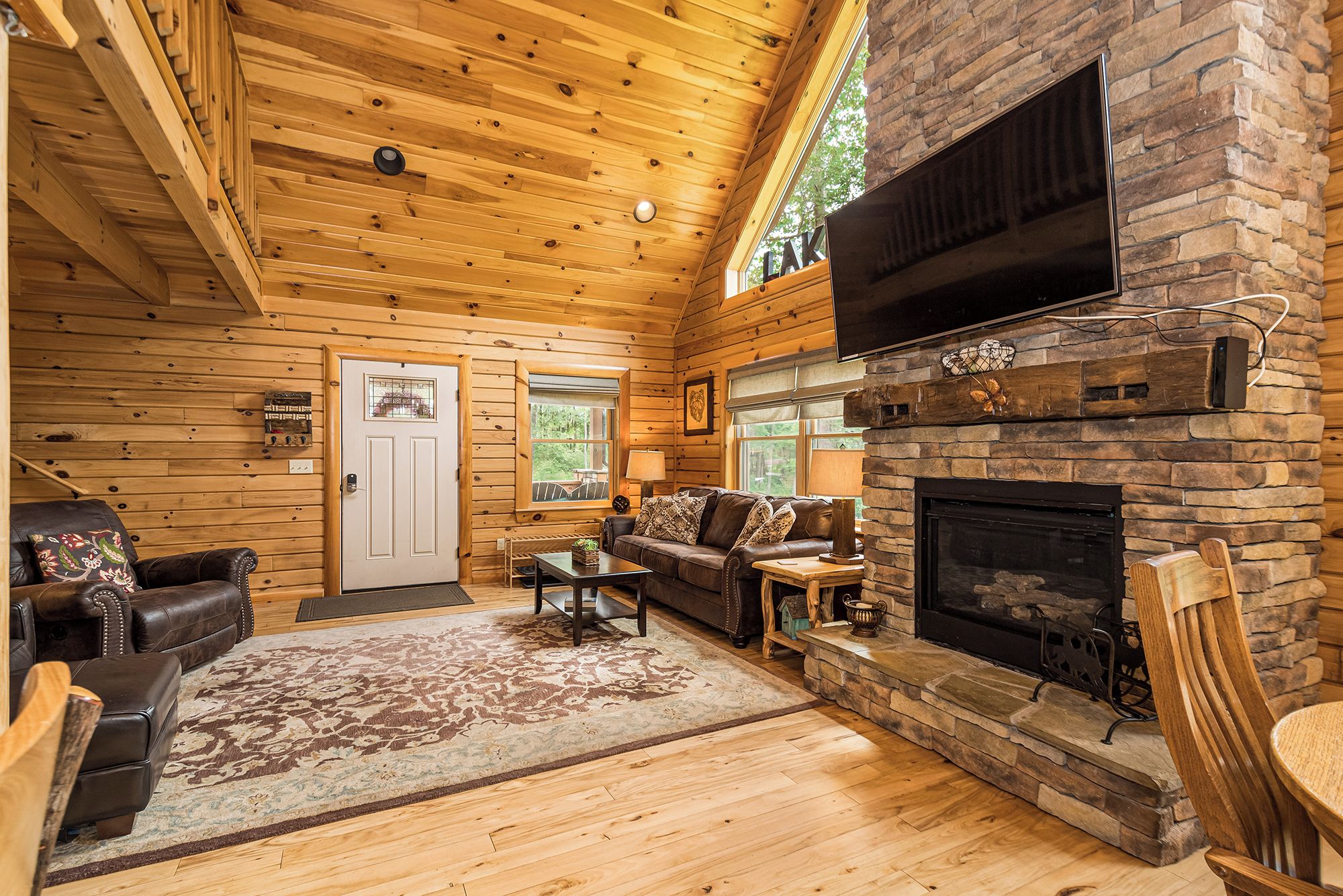A cozy cabin interior with a stone fireplace, wooden walls, and a leather sofa.