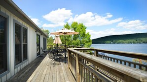 A wooden deck with outdoor furniture and a table, overlooking a body of water and surrounded by trees. - Lucky 12 by Taylor Made Deep Creek (Oakland)