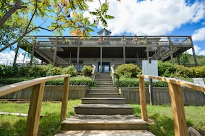 A wooden staircase leading to a covered deck with railings, surrounded by greenery. - Lucky 12 by Taylor Made Deep Creek (Oakland)
