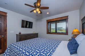 A bedroom with a bed, a ceiling fan, a TV, a window, and a nightstand with a lamp. - Lucky Bear Lakeside by Taylor Made Deep Creek (Swanton)