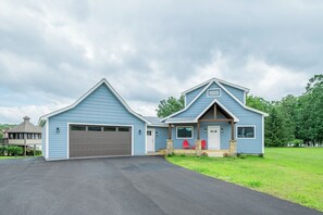 A two-story house with a garage, a front porch with red chairs, and a well-maintained lawn. - Lucky Bear Lakeside by Taylor Made Deep Creek (Swanton)