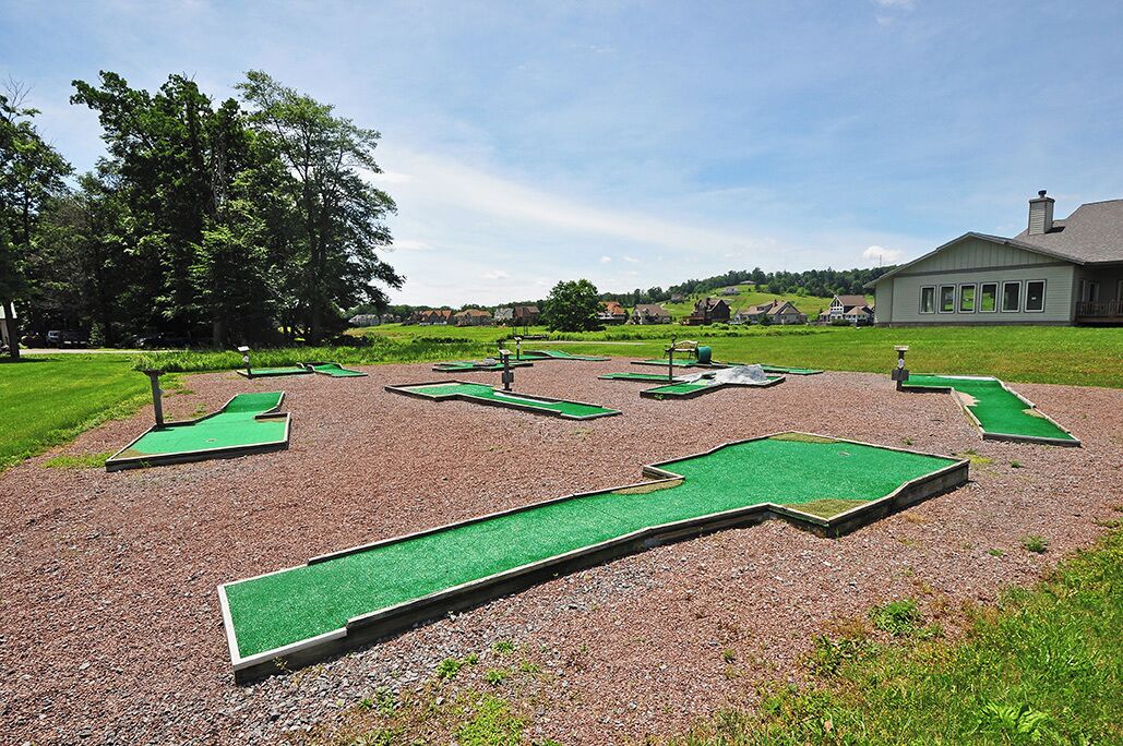 Um campo de mini golfe com vários buracos e uma casa ao fundo.