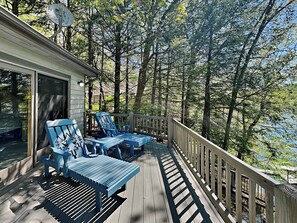Eine Holzterrasse mit blauen Adirondack-Stühlen und einem Tisch, umgeben von Bäumen.