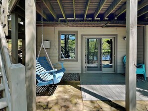 Eine überdachte Veranda mit einer Hängematte, Steinböden und Blick auf einen bewaldeten Bereich durch eine Glastür.